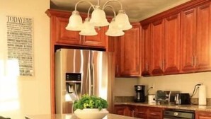 Una cocina con armarios de madera, un refrigerador de acero inoxidable, un horno empotrado, una cafetera y una zona con taburetes de bar.