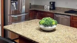 Una cocina con armarios de madera, electrodomésticos de acero inoxidable, encimera de granito y lámpara colgante.