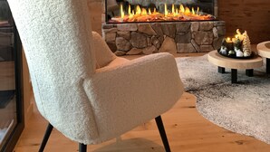 Un salon chaleureux avec une cheminée en pierre, un fauteuil confortable, un téléviseur fixé au mur et une table décorative ornée de bougies.