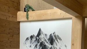 Une pièce avec un grand tableau représentant des montagnes enneigées au mur, un plafond en bois et un canapé gris.