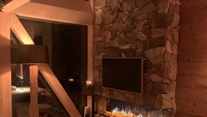 Une cheminée en pierre avec un téléviseur fixé au-dessus, entourée de bougies et agrémentée d’une décoration rustique.
