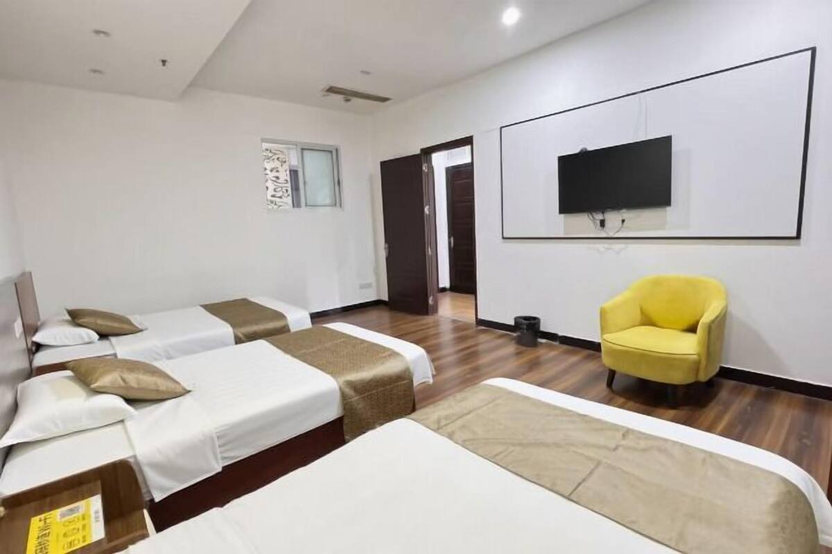 A hotel room with two beds, a yellow armchair, a flat-screen TV, and a small window.