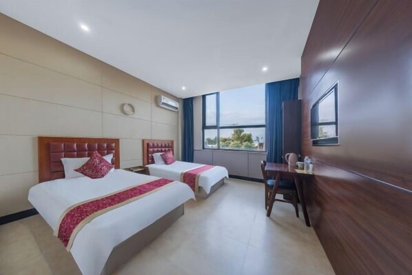 A hotel room with two beds, a desk, and a large window offering a view.
