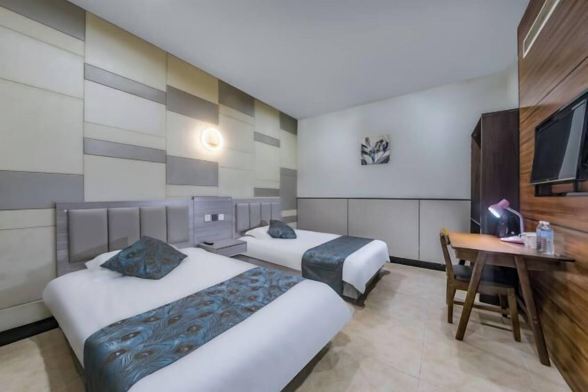 A hotel room with two beds, a desk, and a TV.
