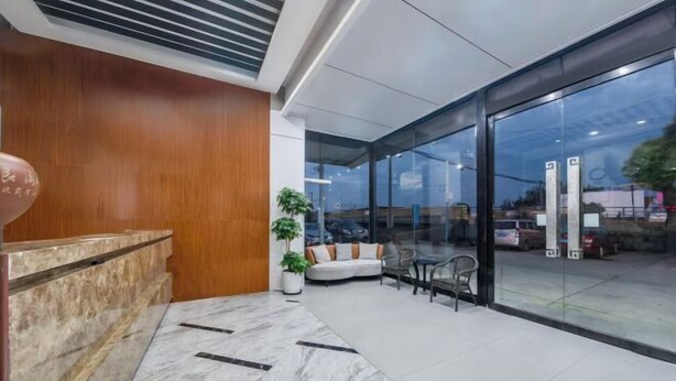 A modern lobby with a marble reception desk, a seating area with a sofa and chairs, and large glass doors leading outside. - Yilang Hotel (Shanghai)