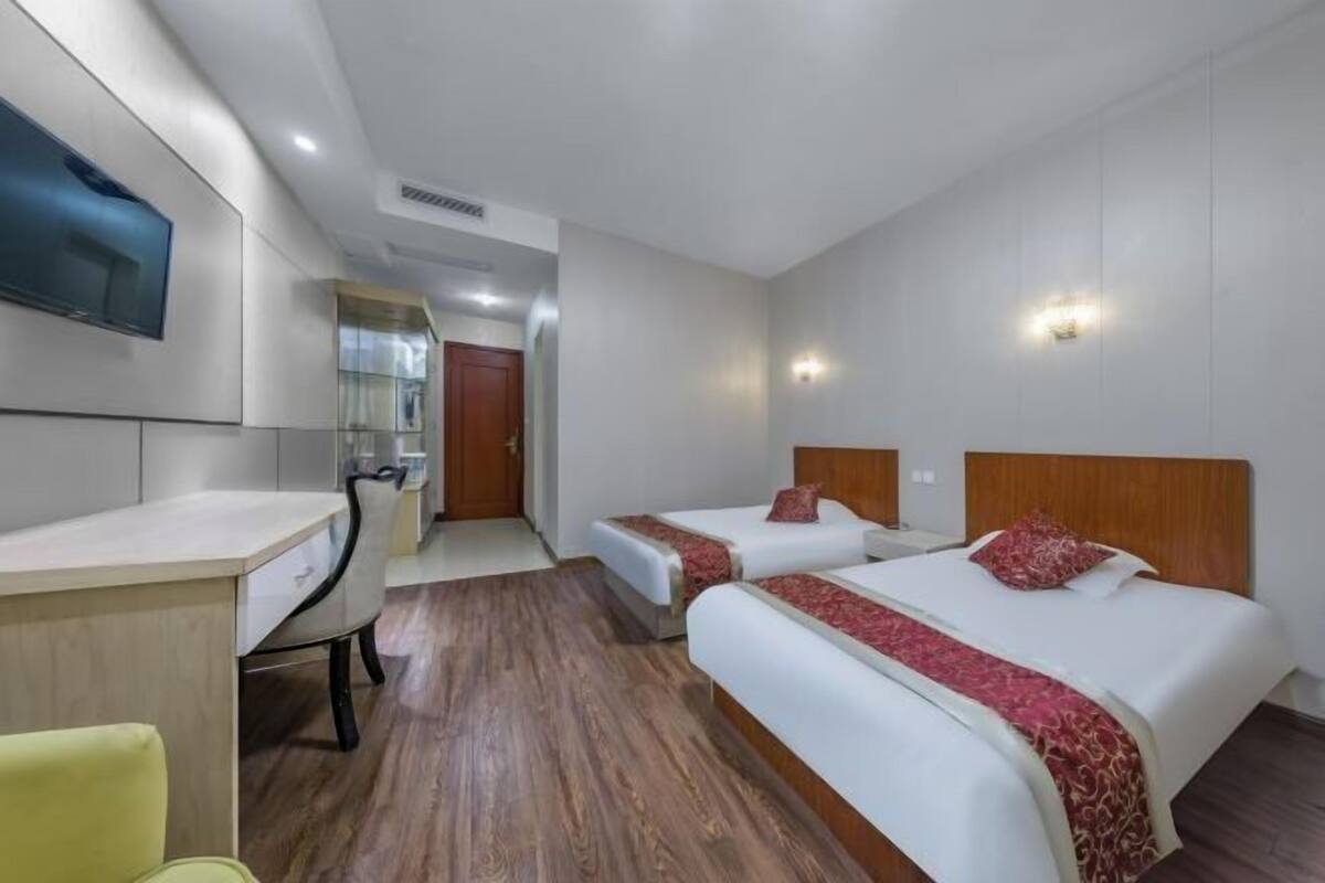 A hotel room with two beds, a desk, a chair, and a TV mounted on the wall.
