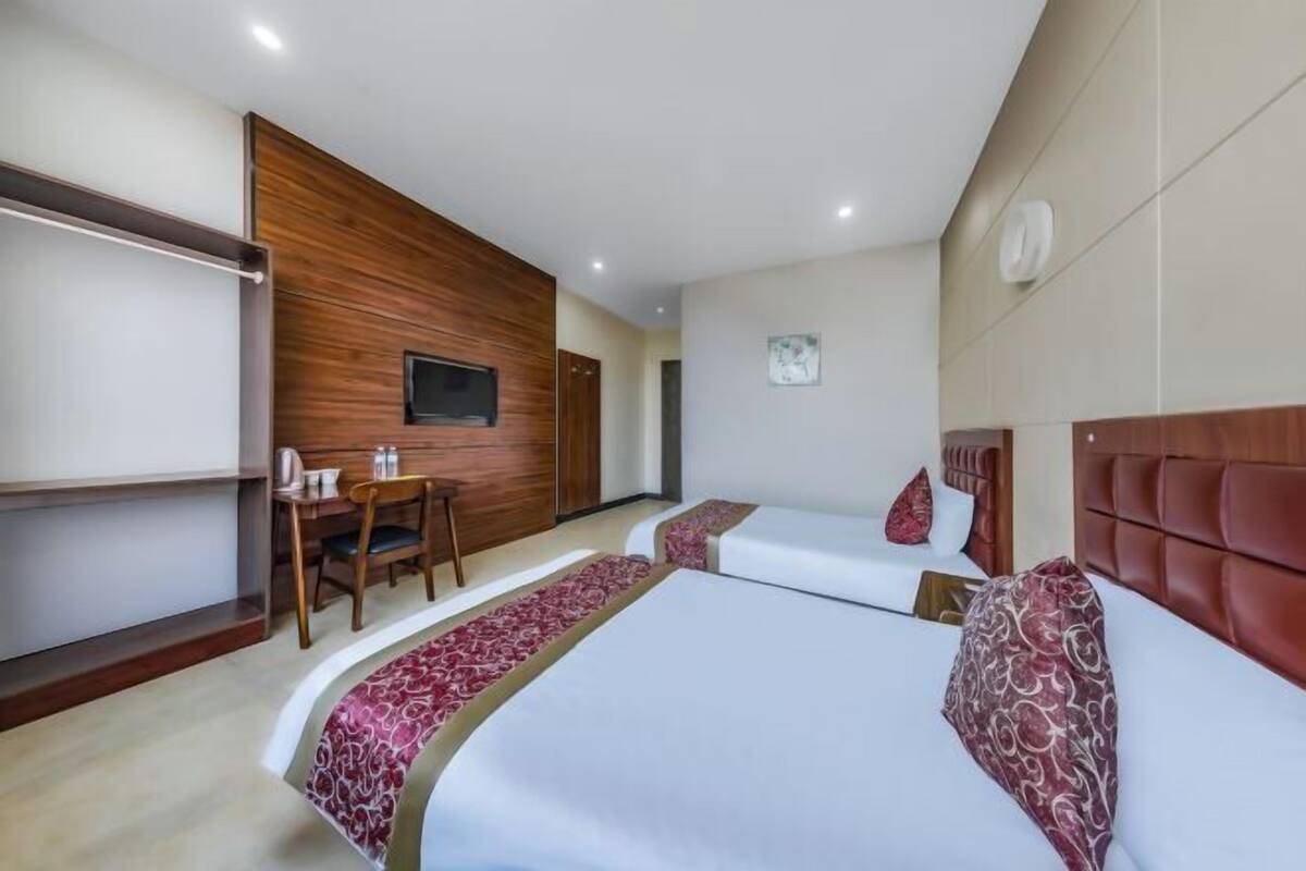 A hotel room with two beds, a desk, and a television.