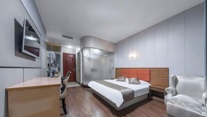 A modern hotel room with a wooden desk, a bed with a grey and white headboard, and a white armchair. - Yilang Hotel (Shanghai)