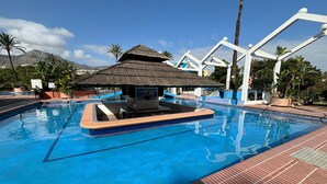 A swimming pool with a small hut, palm trees, and a mountain in the background. - Apartment With sea Views in Benalbeach (Benalmádena)