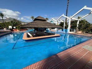 A swimming pool with a small hut, palm trees, and a mountain in the background. - Apartment With sea Views in Benalbeach (Benalmádena)