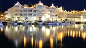 A marina with multiple yachts docked, a large white building with multiple balconies, and a calm water surface reflecting the building and yachts. - Apartment With sea Views in Benalbeach (Benalmádena)