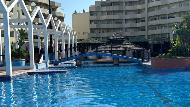 A swimming pool with a bridge, surrounded by buildings and a covered area. - Apartment With sea Views in Benalbeach (Benalmádena)