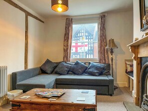A cozy living room with a grey sofa, a wooden coffee table with magazines, a fireplace, and a window with a view of a half-timbered building. - 3 bedroom accommodation in Ashbourne (Ashbourne)
