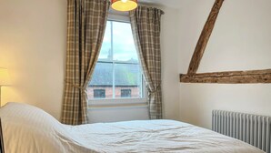 Ein Schlafzimmer mit einem Bett, einem Fenster mit Vorhängen, einem Holzbalken und einer Heizung.