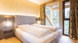 Ein Schlafzimmer mit einer gepolsterten Kopfteile, einem Nachttisch mit Lampe und einem Fenster mit Vorhängen.