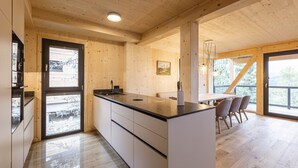 Eine moderne Küche mit Holzwänden und einer großen Kochinsel, ein Essbereich mit Tisch und Stühlen sowie ein Ausblick durch die Fenster.
