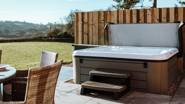 Una vasca idromassaggio con un deck in legno, sedie in vimini e vista sulla campagna.