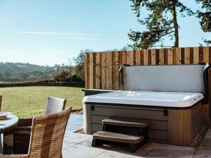 A hot tub with a wooden deck, wicker chairs, and a view of the countryside. - Copper Beech Cottage (Welshpool)