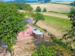 A red brick house with a fenced backyard and a large open field in the background.
