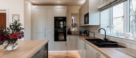 A modern kitchen with white cabinetry, a wooden countertop, a built-in oven, and a window with a view of trees.