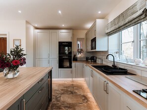 A modern kitchen with white cabinetry, a wooden countertop, a built-in oven, and a window with a view of trees. - Copper Beech Cottage (Welshpool)