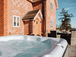 A hot tub in front of a brick house with a dining area and outdoor seating. - Copper Beech Cottage (Welshpool)