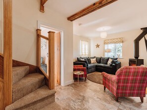 A cozy living room with a fireplace, a red plaid armchair, and a sectional sofa. - Copper Beech Cottage (Welshpool)