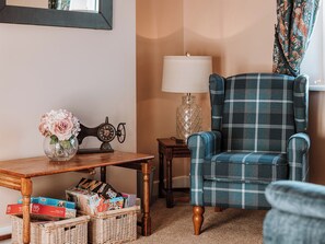 A cozy living room with a plaid armchair, a vintage sewing machine, a vase of flowers, and a table with magazines and books. - Copper Beech Cottage (Welshpool)