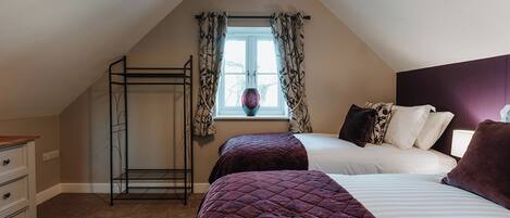 A bedroom with two beds, a window with curtains, a bedside table, and a wardrobe.
