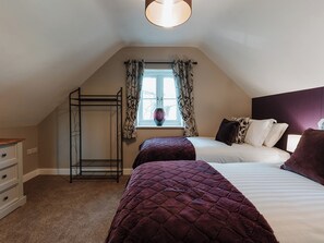 A bedroom with two beds, a window with curtains, a bedside table, and a wardrobe. - Copper Beech Cottage (Welshpool)