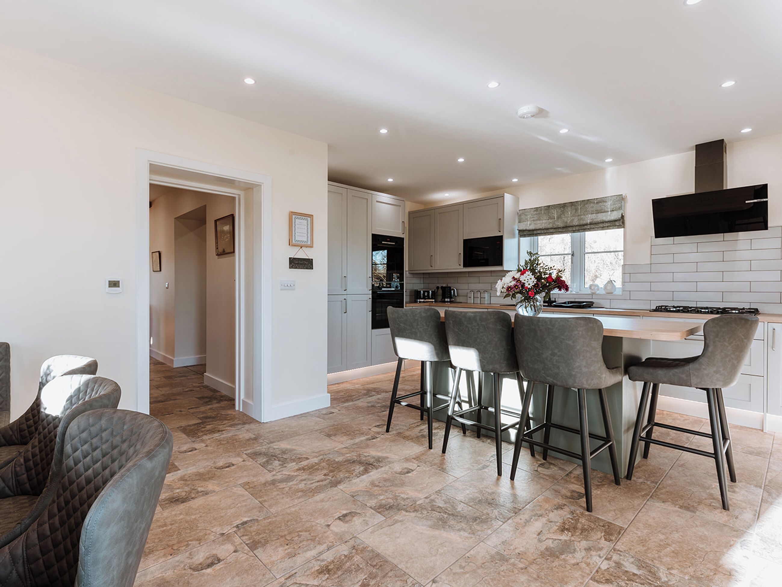 Una cocina moderna con una isla central, taburetes de bar y un área de comedor con una silla acolchada.