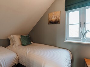 A bedroom with two beds, a window with a view, and a painting on the wall. - Copper Beech Cottage (Welshpool)