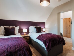 A bedroom with two beds, each with a headboard, bedside tables, and lamps. The room has a sloped ceiling and a wooden door. - Copper Beech Cottage (Welshpool)