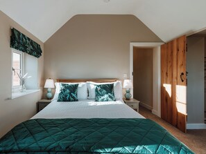 Une chambre avec un grand lit, une fenêtre donnant sur un beau paysage, une table de chevet avec une lampe et une porte en bois.