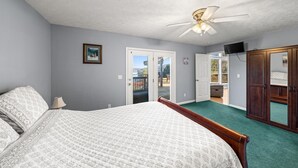 A bedroom with a bed, a ceiling fan, a door leading to a balcony, and a wooden wardrobe.