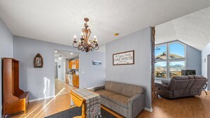 A spacious living room with a high ceiling, a chandelier, a sofa, a recliner, and a view of the outdoors through large windows.