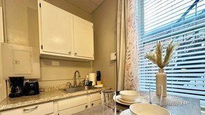A modern kitchen with white cabinets, a granite countertop, a coffee maker, and a dining area with a table set for two.