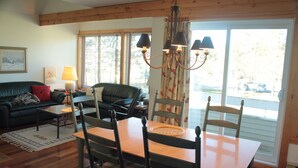 Un salón acogedor con un sofá verde oscuro, una mesa de comedor de madera con sillas, una araña y un ventanal con cortinas.