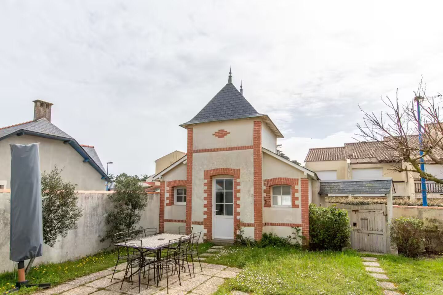 Een huis met een klein torentje, een terras met een tafel en stoelen, en een tuin.