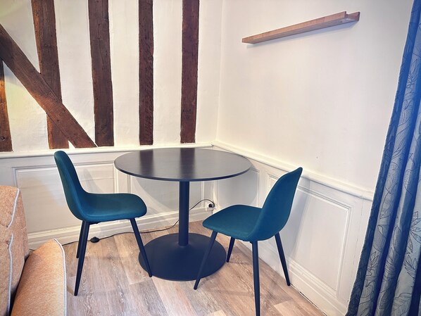 A corner room with a round table and two chairs, wooden beams on the wall, and a shelf above the table. - Charming studio just a stone's throw from the station (Tours)