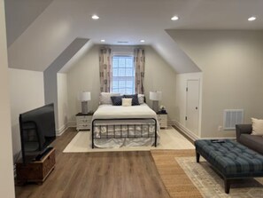 A bedroom with a bed, bedside tables, a TV, a sofa, and a window with curtains.