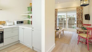 Cocina compacta con gabinetes blancos, microondas y tostadora. Cuenta con un comedor con mesa, sillas y vistas a través de una puerta de vidrio.