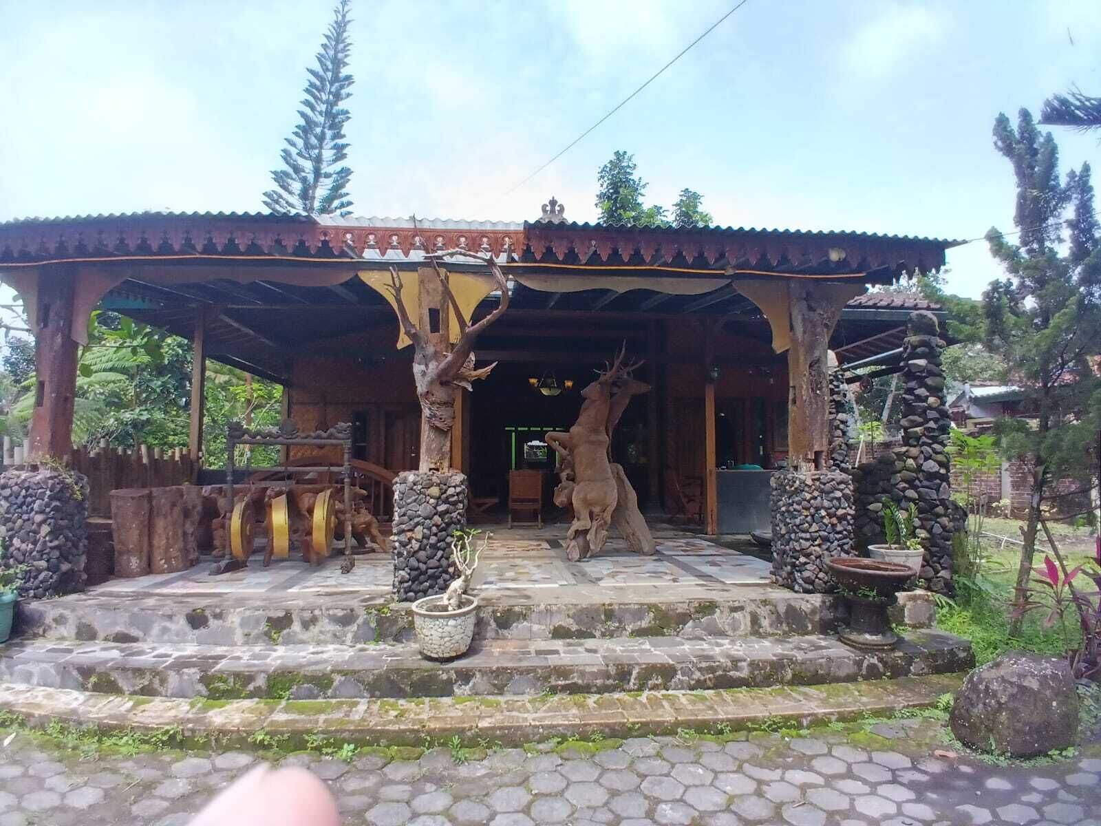 Ein überdachter Eingangsbereich mit Steinstufen, Holzsäulen und einer Hirschstatue.
