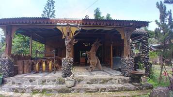 Ein überdachter Eingangsbereich mit Steinstufen, Holzsäulen und einer Hirschstatue.