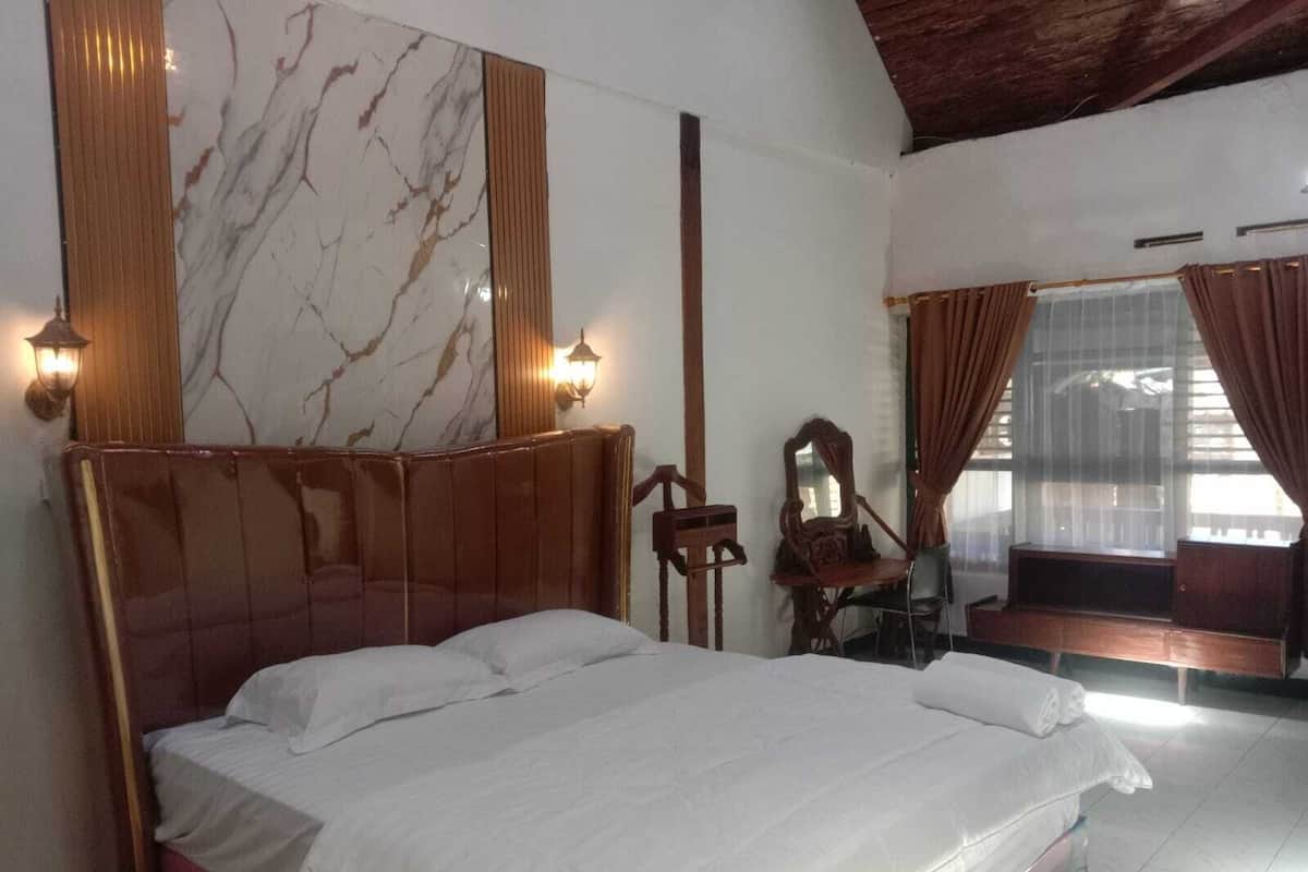 A bedroom with a wooden bed, marble wall, two wall sconces, a chair, and a window with curtains.