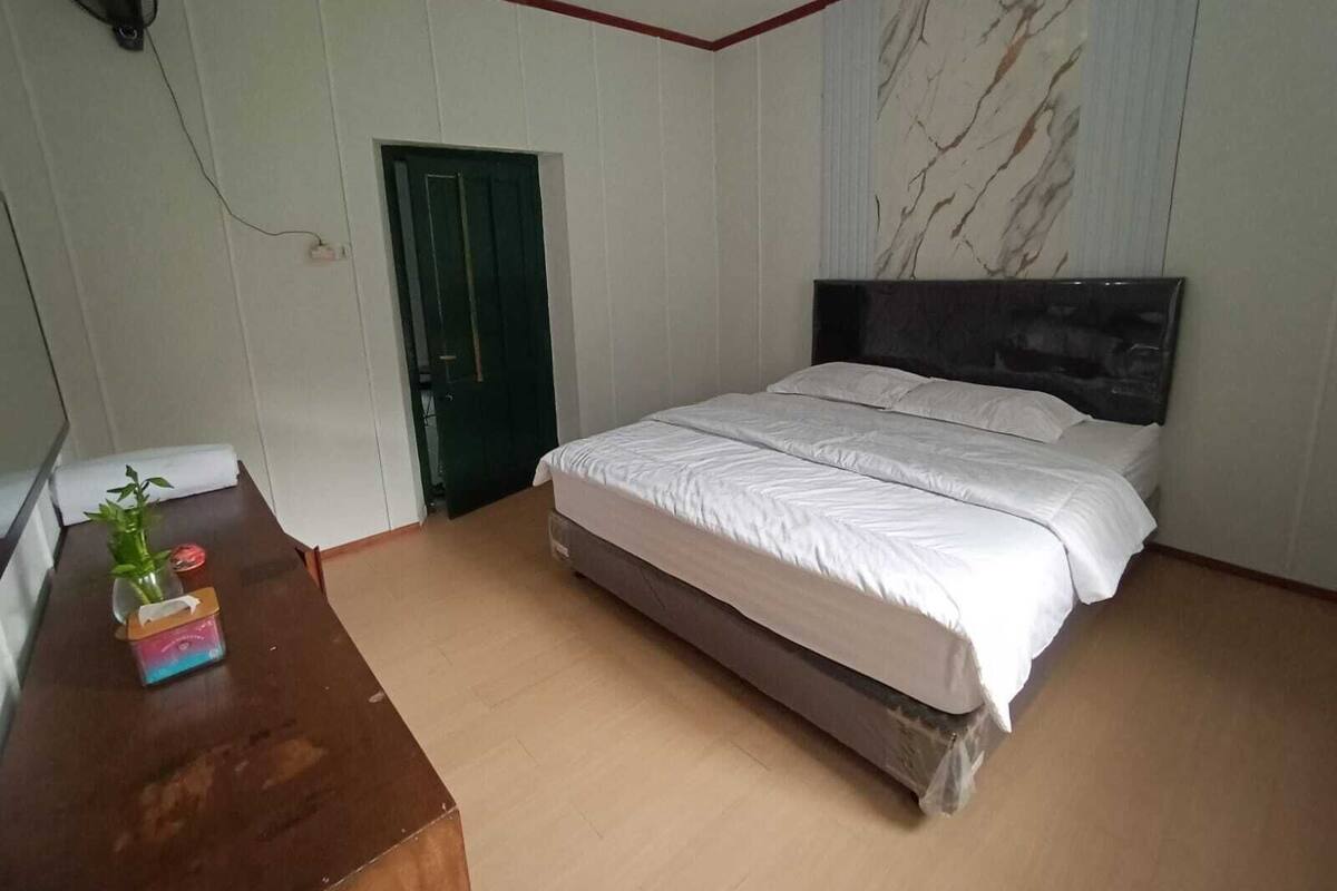A bedroom with a bed, a desk with a plant, a door, and a marble-patterned wall.