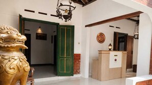 A reception area with a lion statue, a green door, a reception desk, and a doormat with text. - Aurora Living Merapi Jogja (Pakem)
