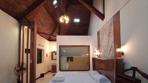 A bedroom with a large bed, a wooden ceiling, a mirror, and a fan. - Aurora Living Merapi Jogja (Pakem)