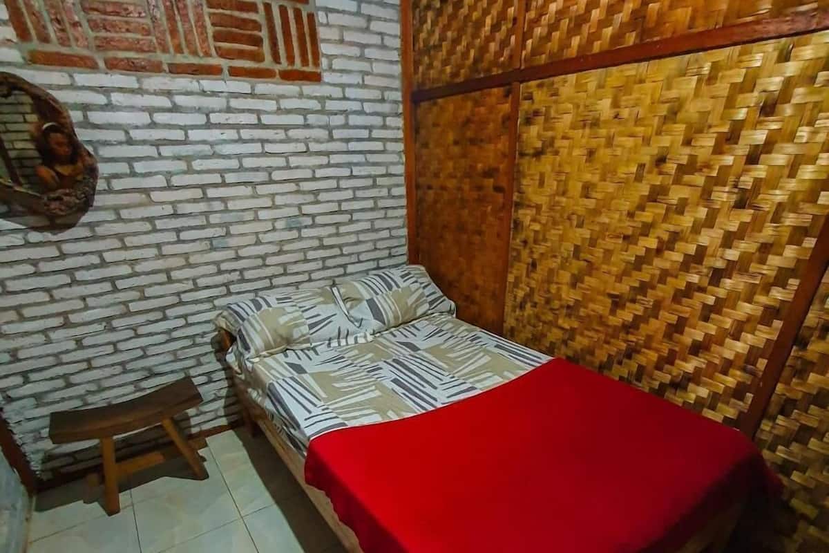A small, neatly arranged bedroom with a single bed, a wooden bench, and a woven wall panel.