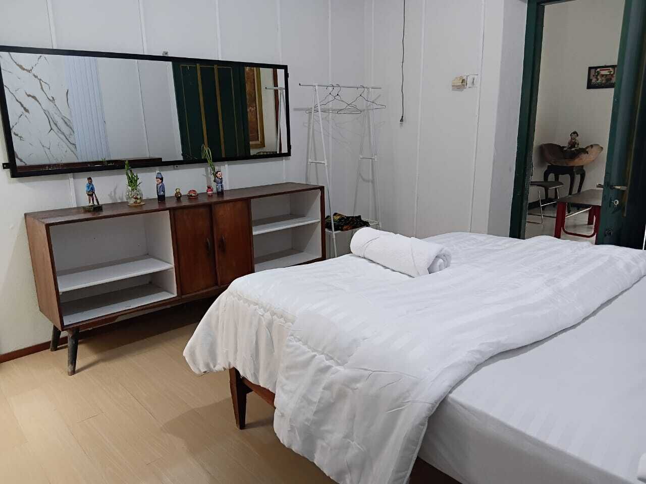 A bedroom with a bed, a wooden wardrobe, a mirror, and a hanging clothes rack.